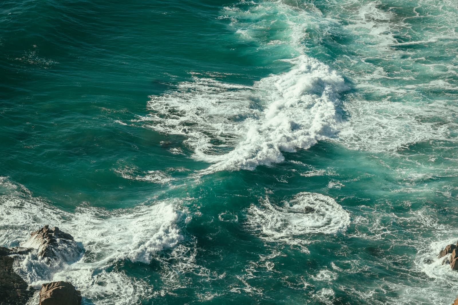 Swirling sea surf along a rocky shore, photographed from above – the ocean’s transport of heat and salt begins at the surface, but the overturning circulation is driven by dense water sinking to depth