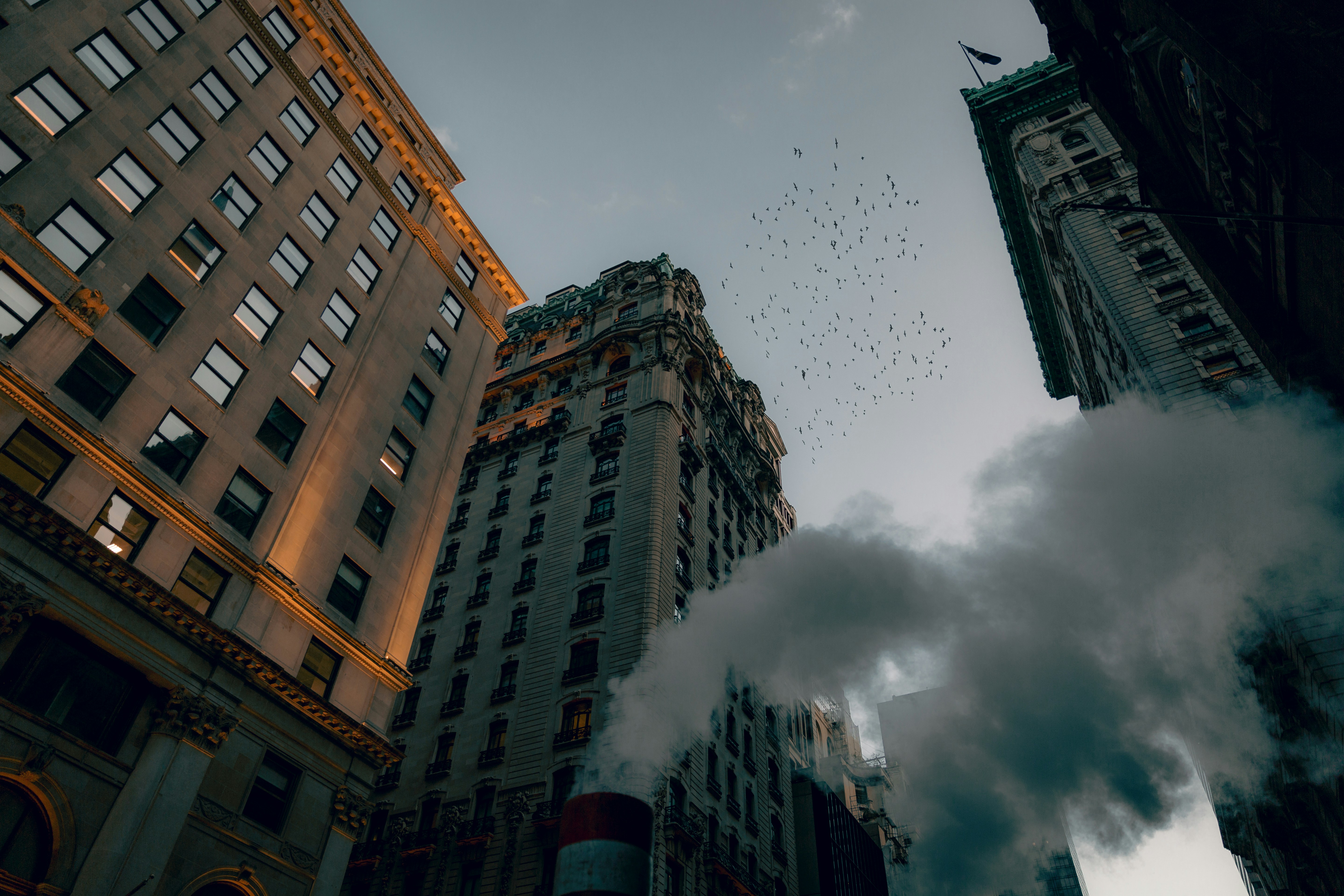 Low-angle view of historic city buildings with large steam and smoke plumes rising from the street - anthropogenic heat release and steam infrastructure in the dense urban fabric, illustrating the thermal burden of the built environment
