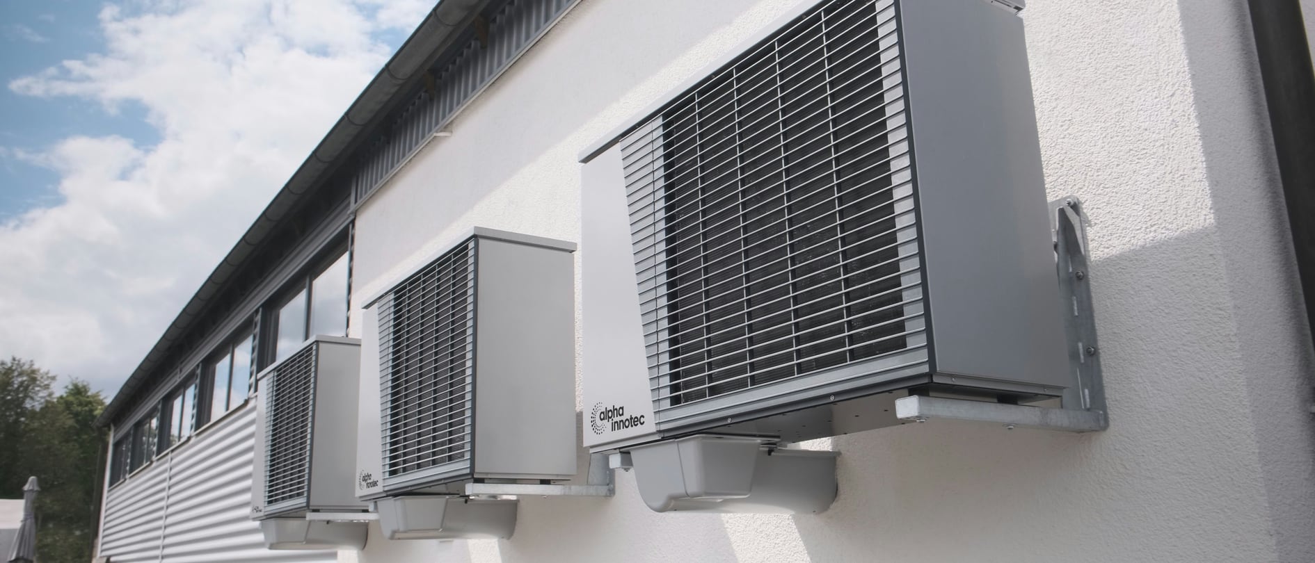 Three wall-mounted air-to-water heat pump outdoor units on a rendered building facade – the thermal condition of the envelope determines the temperature level at which this plant has to work