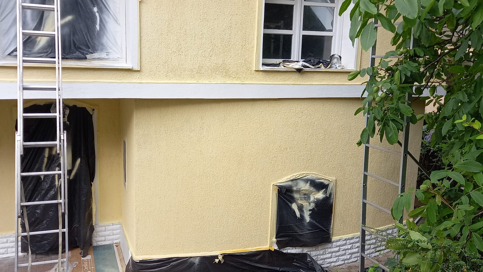 Family house with a pale yellow facade being coated with GWR NANO INSULATION®, openings masked with protective sheeting, Budapest District III